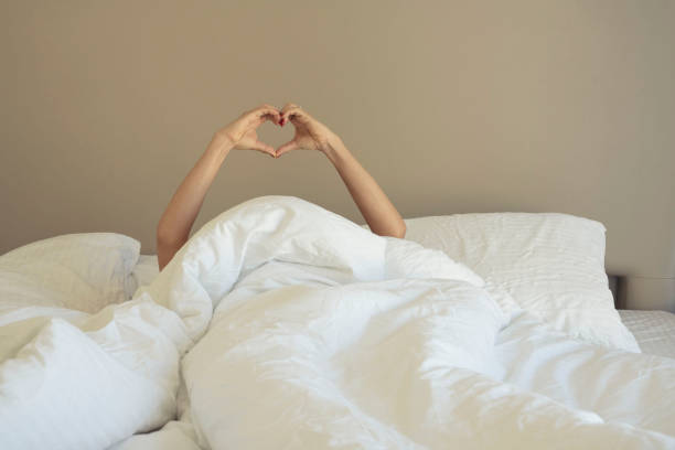 istock Woman hands making heart shape lying in bedroom 1195851157