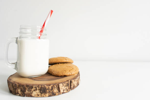 Old fashion milk jar and mason jar with red striped straws and oatmeal cookies on white background. christmas theme milk and cookies stock photo