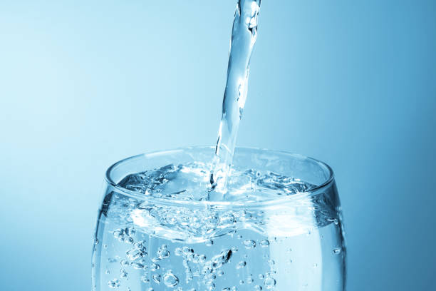 Derramar a água em um vidro no fundo azul - foto de acervo