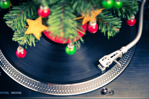 Senior Bearded Man Wearing Headphones Carefully Placing A Vinyl Record On A Vintage Turntable In A Workshop Environment, Expressing Nostalgia, Love For Analog Music And Retro Lifestyle Surrounded By Tools And Festive Lights.