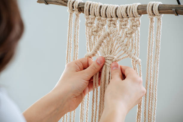 Craftswoman weving ropes, creating a macrame banner. from behind. Brunette woman working on a half-finished macrame piece, weaving ropes, making knots. Close up. Cropped. From behind. macrame stock pictures, royalty-free photos & images