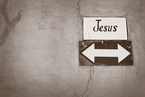Jesus road sign arrow on a cracked concrete wall. Concept for doubt in religion