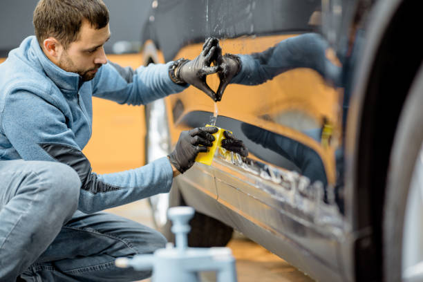 Filming car body at the vehicle service Car service worker sticking anti-gravel film on a car body with scrapper at the detailing vehicle workshop. Concept of car body protection with special films black shawl wrap stock pictures, royalty-free photos & images