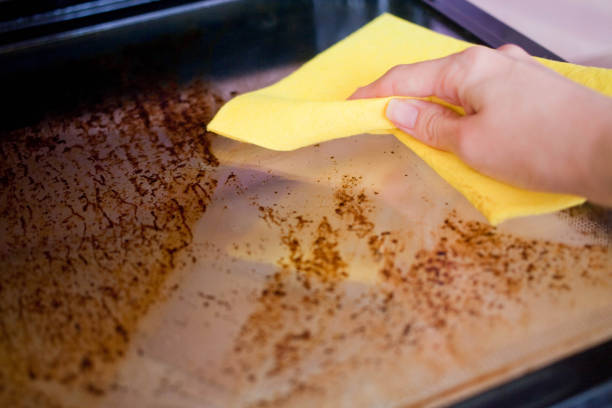 a female hand is holding a yellow rag and washing the dirty door of the oven. - oven imagens e fotografias de stock