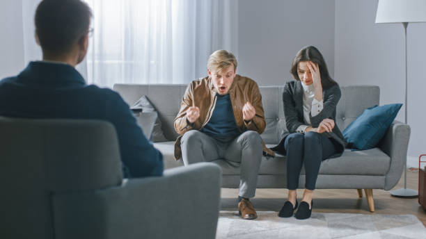 jeune couple sur la session de conseil avec le psychothérapeute. back view of therapist taking notes: angry boyfriend loses temper, starts to shout at his suffering girlfriend. violence domestique - violence married therapy solution photos et images de collection