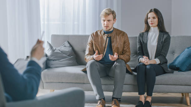 jeune couple sur la session de conseil avec le psychothérapeute. back view of therapist taking notes: angry boyfriend perd temper. violence domestique - violence married therapy solution photos et images de collection