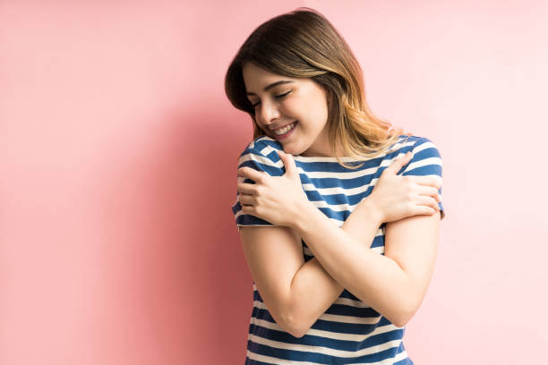 She Loves Herself Against Colored Background Charming happy young woman hugging herself while isolated against pink background hugging self stock pictures, royalty-free photos & images