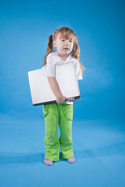 La petite fille est en tenant un ordinateur sur le bleu - Photo