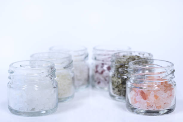 Several jars filled with different types of salt stand side by side against a white background with space for text
