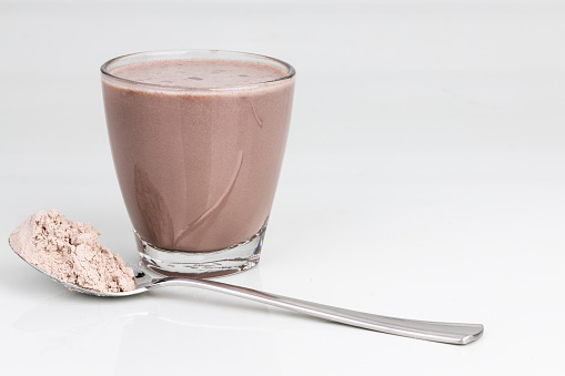Chocolate flavored protein drinks in glass with scope of protein powder for nutrients and energy