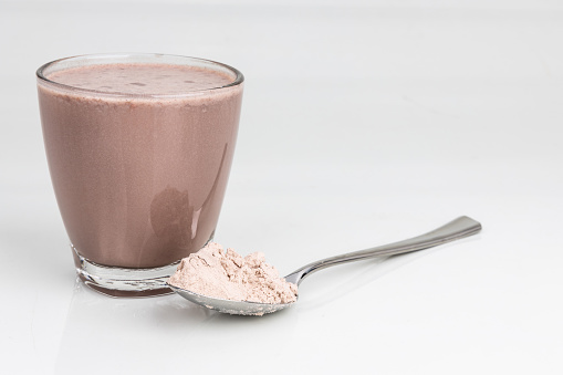 Chocolate flavored protein drinks in glass with scope of protein powder for nutrients and energy