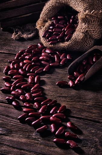Close-up low key image of red beans or kidney beans in burlap sack on rustic wooden table