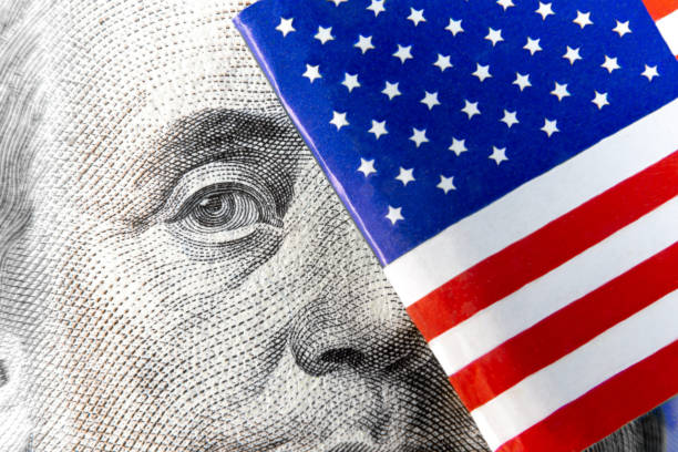 istock Extreme macro of Benjamin Franklin from one hundred dollar banknote hiding out behind micro flag of USA. Real photo. 1195916561