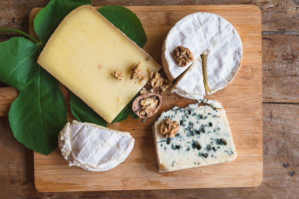 Various french cheeses, nuts, fig leaf on the wooden cutting board.