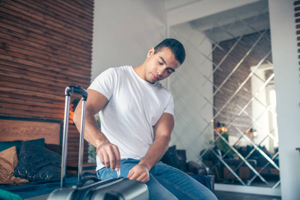 istock Dark-haired young man in white tshirt zipping his suitcase 1195921951