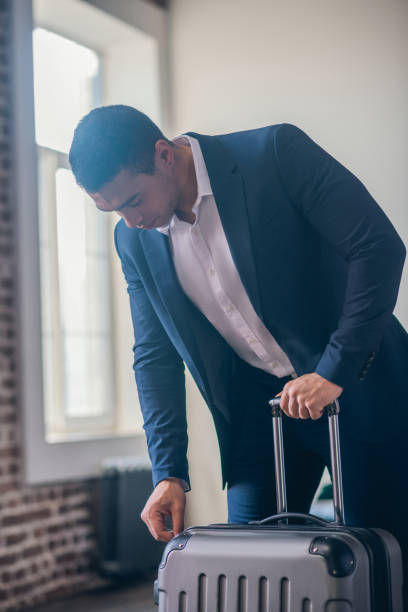istock Dark-haired young man in elegant suit zipping his suitcase 1195921979