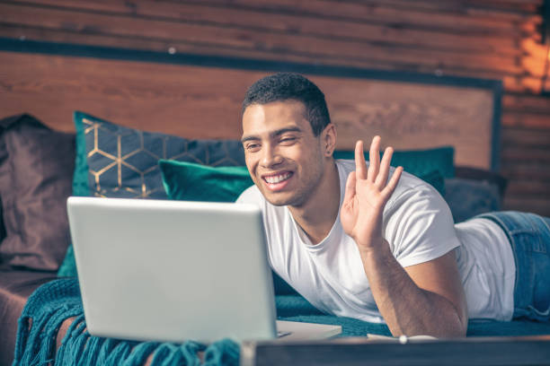 istock Cheerful guy greeting online in front of laptop screen. 1195922540