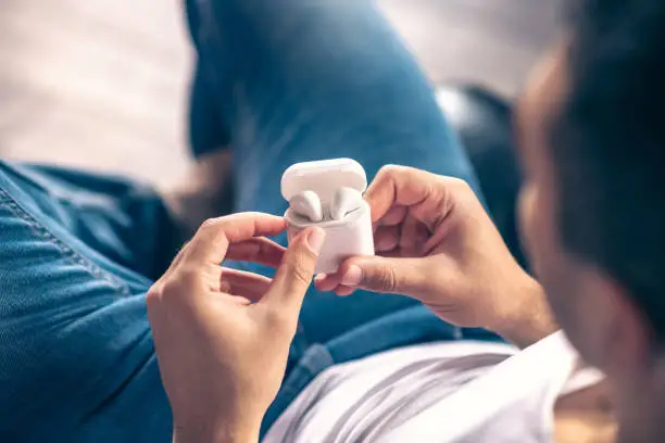 Stylish gadget. Stylish wireless white headphones in the hands of a sitting guy.