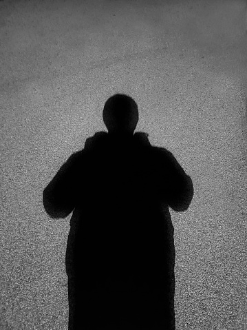 Silhouette of a man projected on the sidewalk. The concept of loneliness, secrecy. The concept of espionage, tracking, viruses.