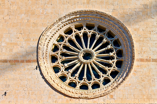 L'Aquila, Abruzzo, Italy. Close-up of the large rose window on the pink stones facade of the church of San Silvestro, after the restoration from the damage of the 2009 earthquake. Made in the fourteenth century, it is in Romanesque style with Gothic influences.\nThe oblique shadow that cuts it above is from the crane of the building's restoration site that overlooks the church square.