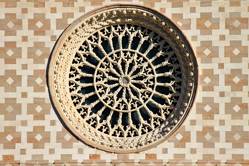 L'Aquila, Abruzzo, Italy. Detail of the central rose window set in the two-colored design of the facade decorated with characteristic motifs of the so-called Aquila cross. The basilica was reopened to the public in December 2017, repaired from the serious damage suffered by the 2009 earthquake.