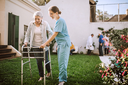 Female nurse helping senior woman with mobility walker at nursing home