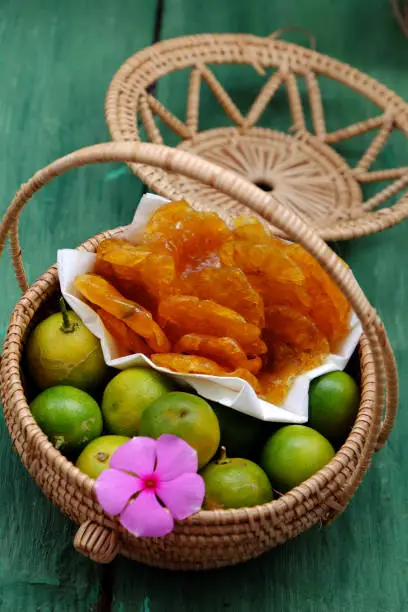 Vietnamese traditional food for tet holiday, close up yellow round kumquat jam and raw material in basket on green wooden background, homemade sweet snack food from fruits for tea time in spring