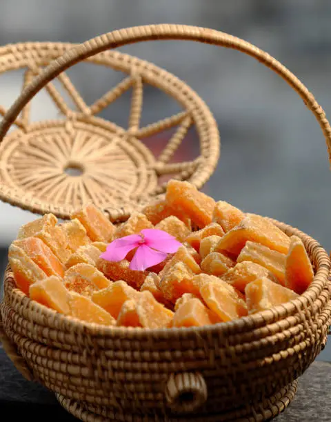 Vietnamese traditional food for Tet holiday, close up yellow sweet potato jam in basket on grey wooden background, delicious sweet snacks for tea time from high view