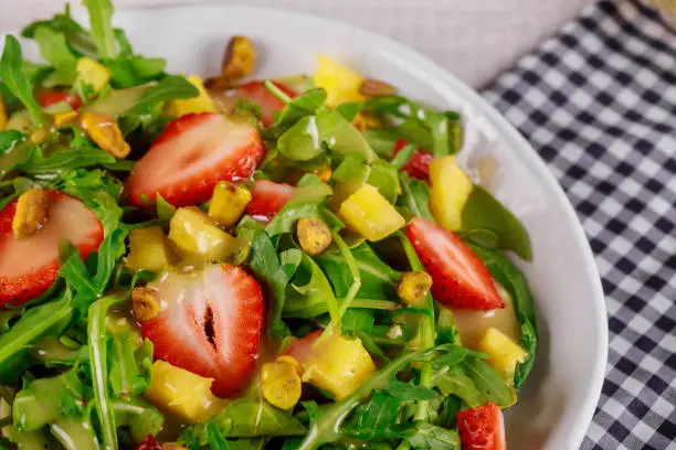 Photo of Green fresh salad with arugula, strawberries, mango and pistachios. Close up.
