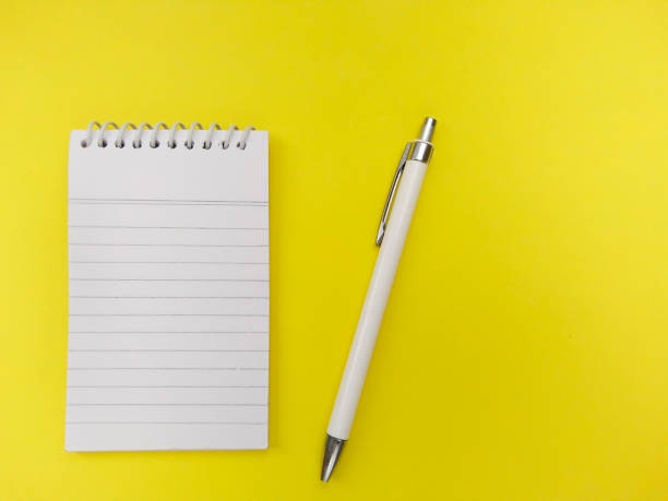istock Spiral notepad diary and pen isolated on yellow colored background. 1195984317