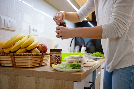 Close-up of unrecognizable woman opening jam jar in kitchen in order to make peanut butter and jelly sandwiches