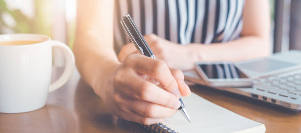 istock Business woman writing on a notepad with a pen and working at a compute. 1195994623