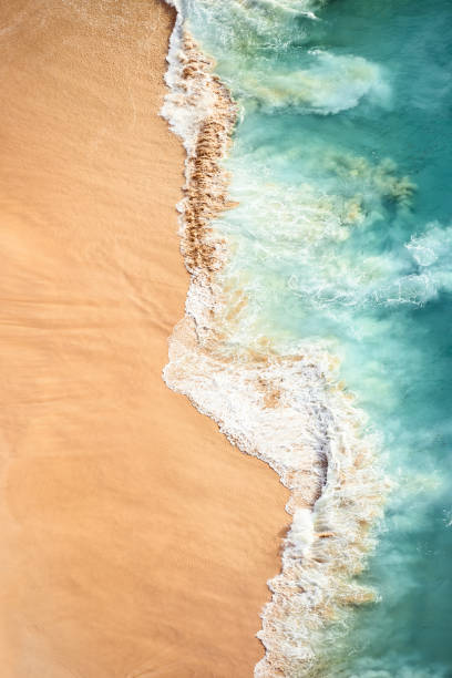 vue d'en haut, vue aérienne imprenable de quelques vagues s'écrasant sur une belle plage pendant le coucher du soleil. plage de kelingking, nusa penida, indonésie. - sand wave pattern beach wave photos et images de collection