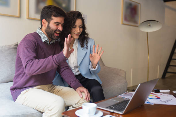 istock Happy couple waving hello at computer screen 1195999029