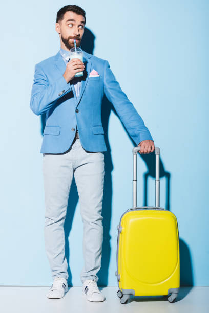 istock man drinking cocktail and holding travel bag on blue background 1196000831