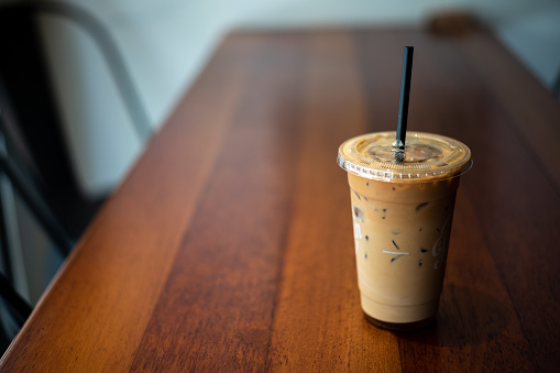 Iced cafe latte in disposable take away cup on top of wooden table