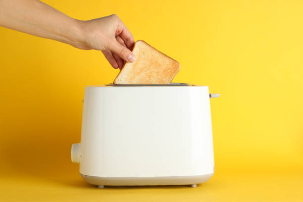 istock Female hand puts bread in a toaster on yellow background, space for text 1196004374