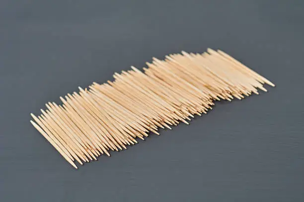 Photo of Row of wooden toothpicks lies on black concrete desk on kitchen. Close-up