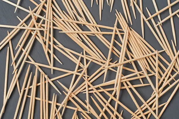 Photo of Scattered wooden toothpicks lies on black concrete desk on kitchen. Top view. Close-up