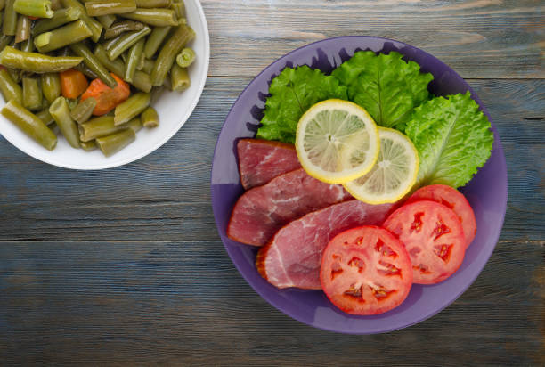 ham with salad, tomato and lemon on a purple  plate. ham on a wooden background .ham top view