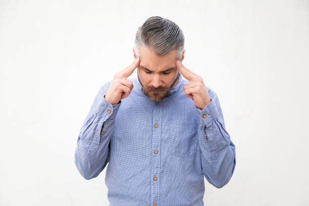 Focused man with closed eyes touching temples, suffering from headache. Grey haired young man in blue casual shirt posing isolated over white background. Stress concept