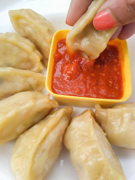 istock Hand dipping momos (dumpling) in red momo chutney. 1196009652