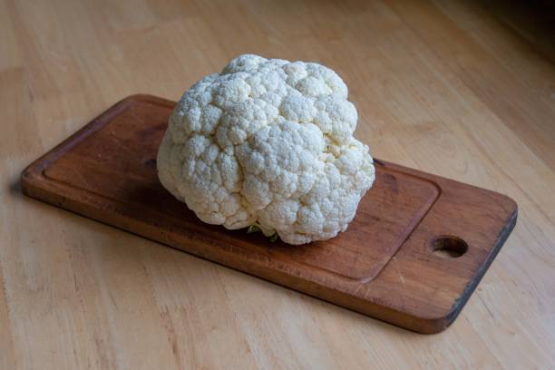 istock Cauliflower with a cutting board on a light wood table. 1196011609