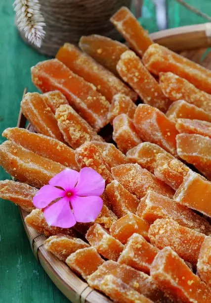 Vietnamese traditional food for Tet holiday, close up yellow sweet potato jam in basket on green wooden background, delicious sweet snacks for tea time from high view