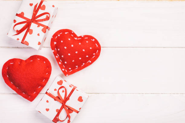 Valentine or other holiday handmade present in paper with red hearts and gifts box in holiday wrapper. Present box gift on white wooden table top view with copy space, empty space for design. san valentín u otro regalo de vacaciones hecho a mano en papel con corazones rojos y caja de regalos en envoltorio de vacaciones. regalo de la caja presente en la vista superior de la mesa de madera blanca con espacio de copia, espacio vacío para el dise