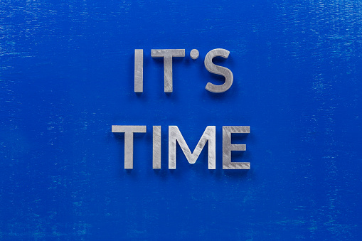 The phrase its time laid on blue painted board with thick silver metal aphabet characters., centered composition concept