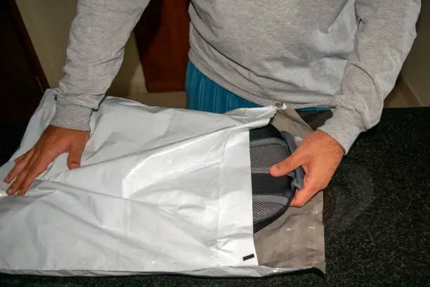 Photo of Man opening plastic parcel delivery with a new backpack