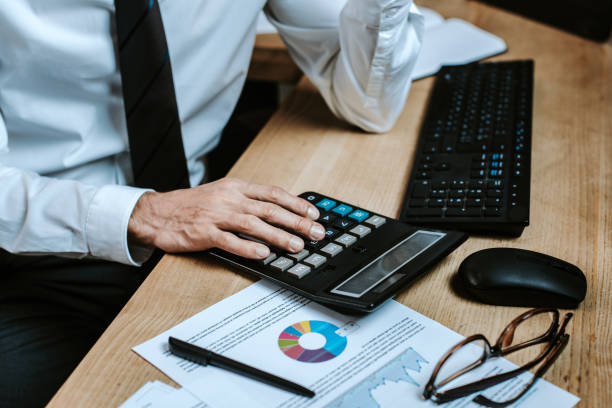 istock cropped view of bi-racial trader using calculator and sitting at table 1196043158