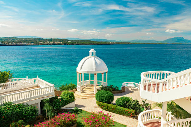 Beautiful white gazebo and tropical flower garden on Caribbean ocean background, summer mountain view , Sosua, Puerto Plata, Dominican Republic Beautiful white gazebo and tropical flower garden on Caribbean ocean background, summer mountain view , Sosua, Puerto Plata, Dominican Republic pavilion photos stock pictures, royalty-free photos & images