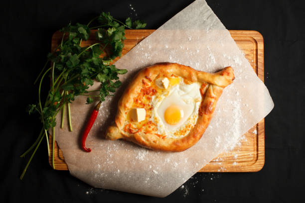 traditionelle georgische gericht khachapuri ajarian im schwarzen hintergrund. frisch gebackenkhachapuri. nationales georgisches gebäck mit käse und rohen eiern - ajaria stock-fotos und bilder